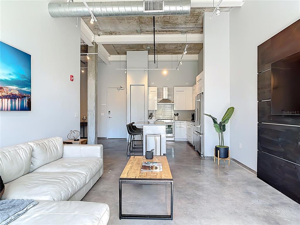 An open-concept living room and kitchen feature concrete ceilings, polished floors, and modern white cabinetry — 302 SE BROADWAY STREET UNIT 240, OCALA, FL
