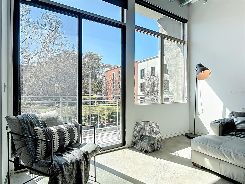 A modern living room features floor-to-ceiling windows, concrete floors, and a view of buildings — 302 SE BROADWAY STREET UNIT 240, OCALA, FL