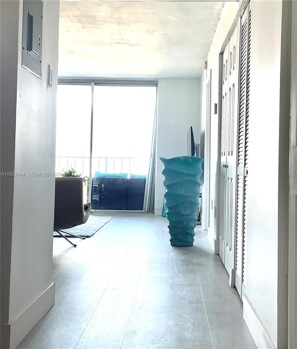 A hallway with light wood-look flooring leads toward a living area with a balcony — 6900 Bay Dr # 7A, Miami Beach FL 33141, MIAMI BEACH, FL