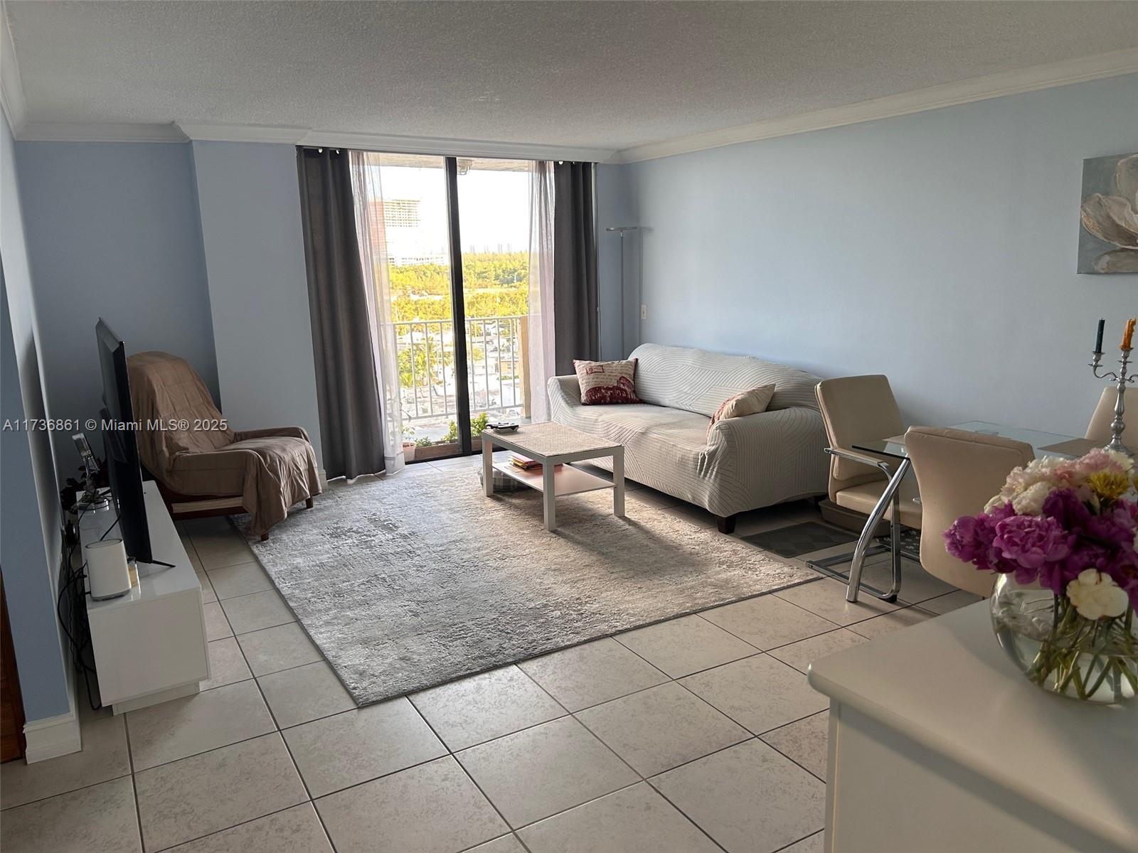 A living room with tile floors, a sofa, a television, and a balcony view — 2350 NE 135th St # 903, North Miami FL 33181, NORTH MIAMI, FL