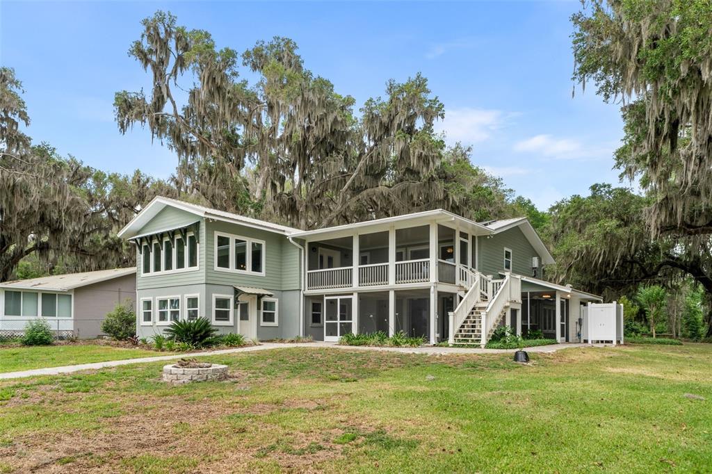 A two-story green house with a metal roof sits near a lake under mossy trees — 8026 NE 221ST STREET, MELROSE, FL
