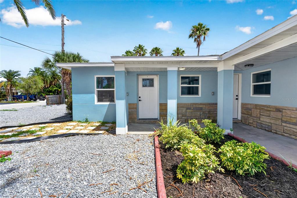 The exterior of a light blue house features a covered entryway and stone accents — 14013 MARGUERITE DRIVE, MADEIRA BEACH, FL