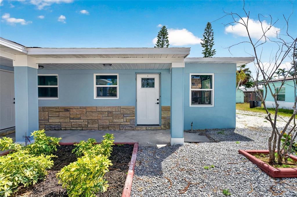 The exterior of a light blue house features a covered porch with stone accents — 14013 MARGUERITE DRIVE, MADEIRA BEACH, FL