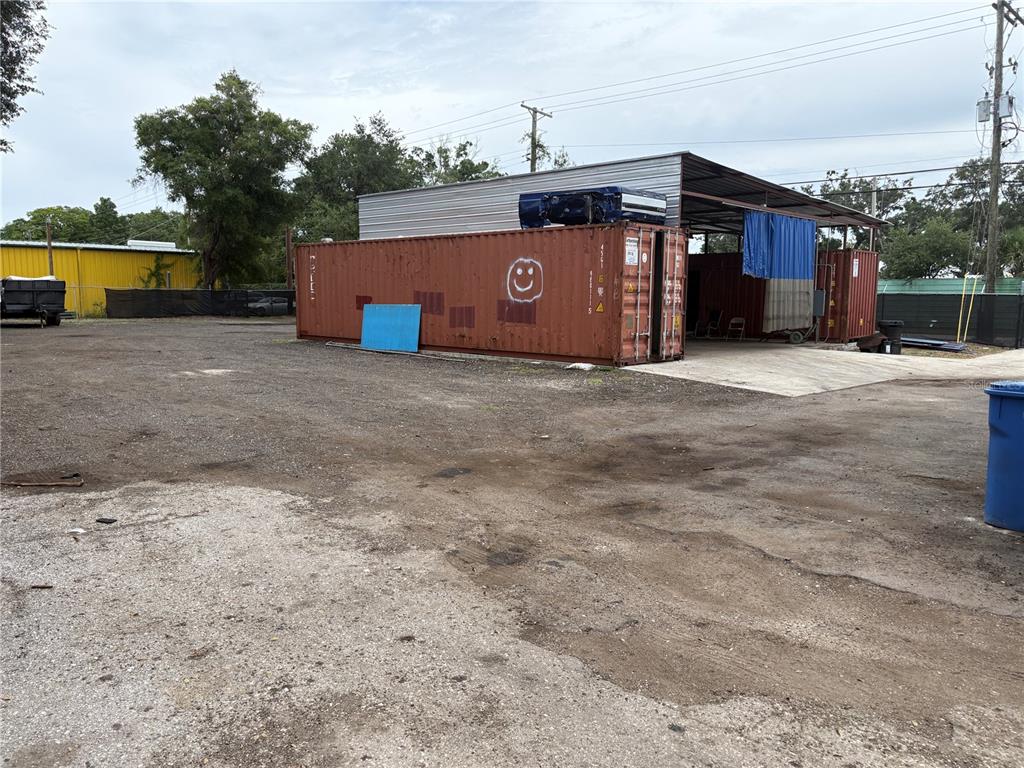 A gravel lot features a red shipping container with a smiley face and a metal structure — 6901 BENJAMIN ROAD, TAMPA, FL