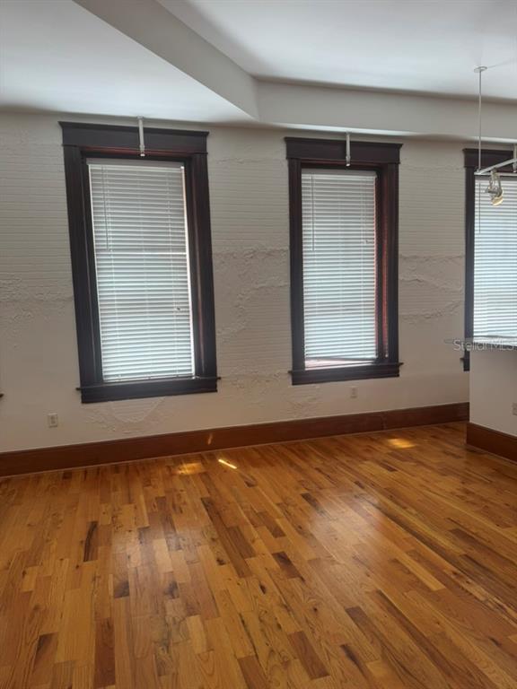 An empty room features hardwood floors, two windows with dark wood trim, and textured walls — 1229 N FRANKLIN STREET UNIT J, TAMPA, FL