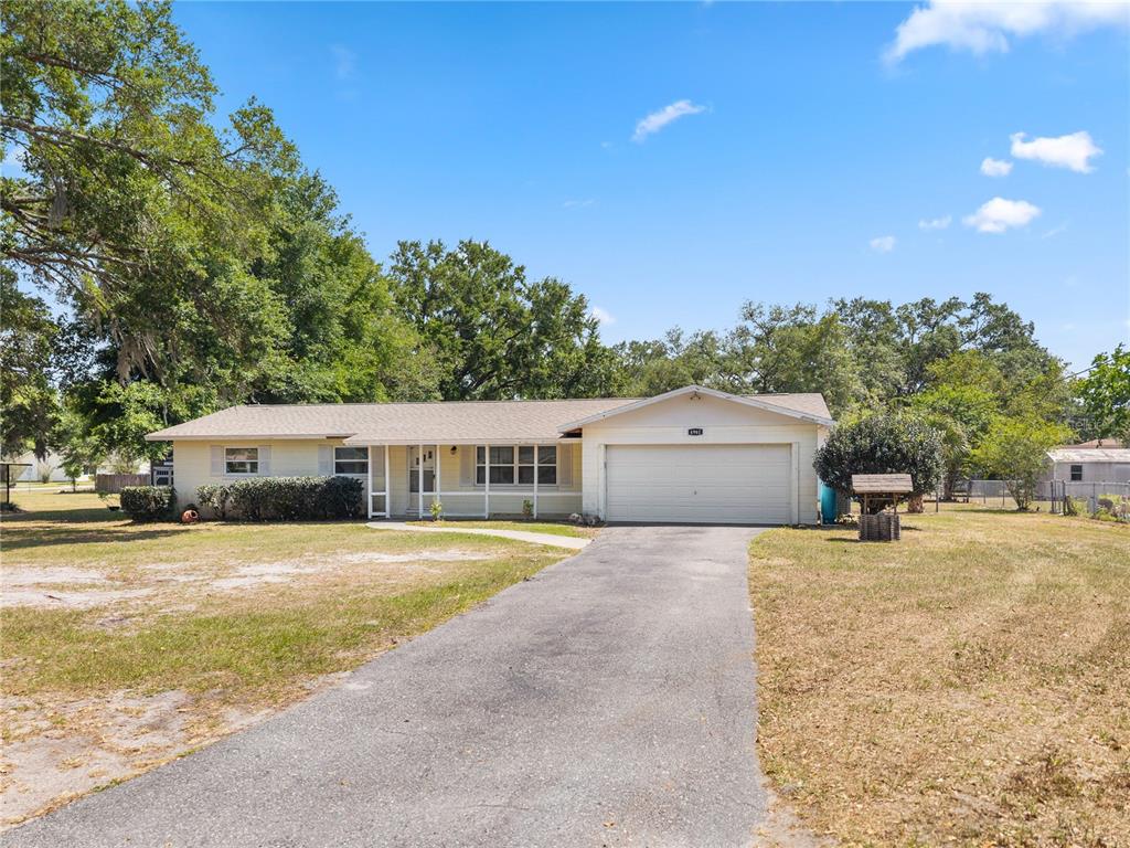 A single-story house with a light-colored exterior, a two-car garage, and a long driveway — 4961 COUNTY ROAD 114, WILDWOOD, FL