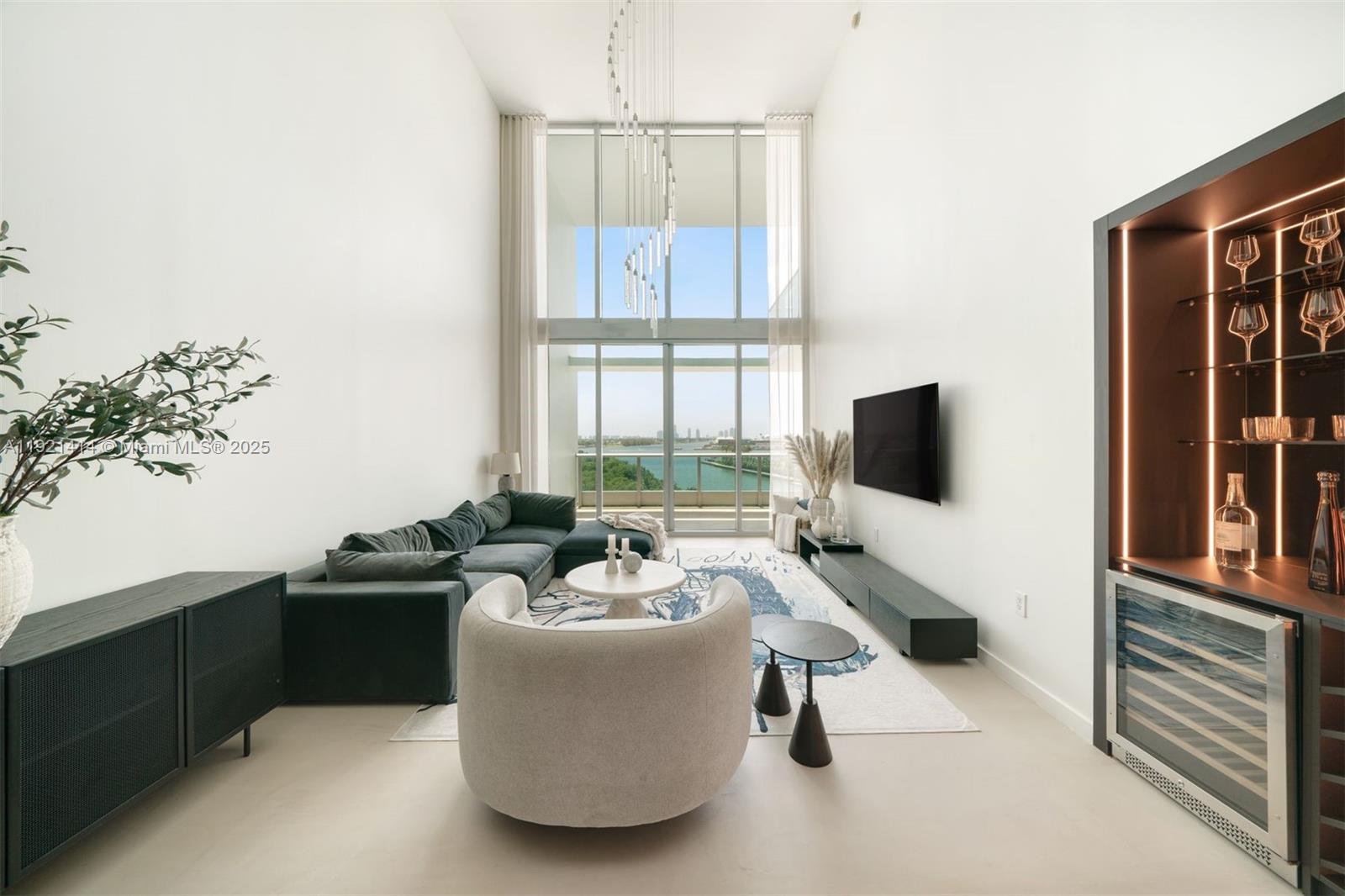 A modern living room features double-height windows, a sectional sofa, and a built-in bar cabinet — 900 Biscayne Blvd # 905, Miami FL 33132, MIAMI, FL