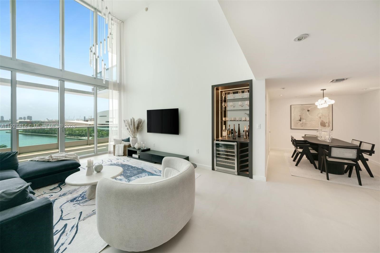 A modern living and dining area features floor-to-ceiling windows, a built-in bar, and white floors — 900 Biscayne Blvd # 905, Miami FL 33132, MIAMI, FL