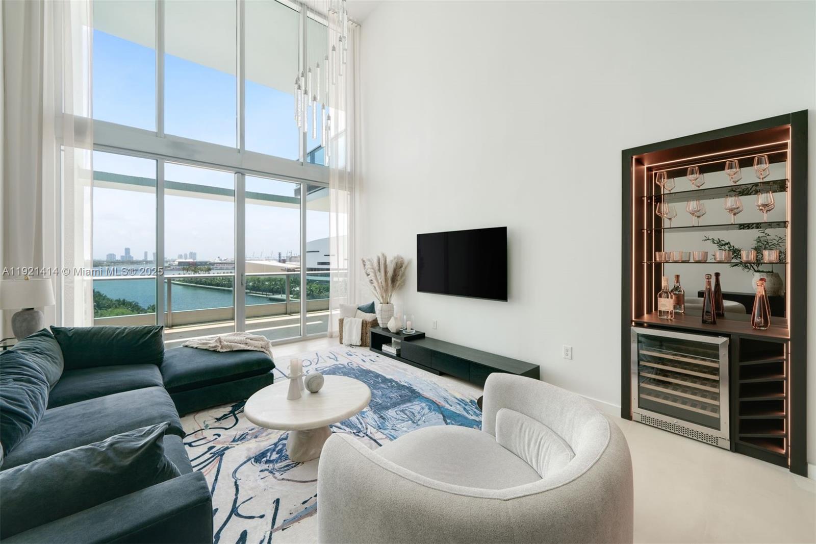 A modern living room features a double-height window, a sectional sofa, and a built-in bar — 900 Biscayne Blvd # 905, Miami FL 33132, MIAMI, FL