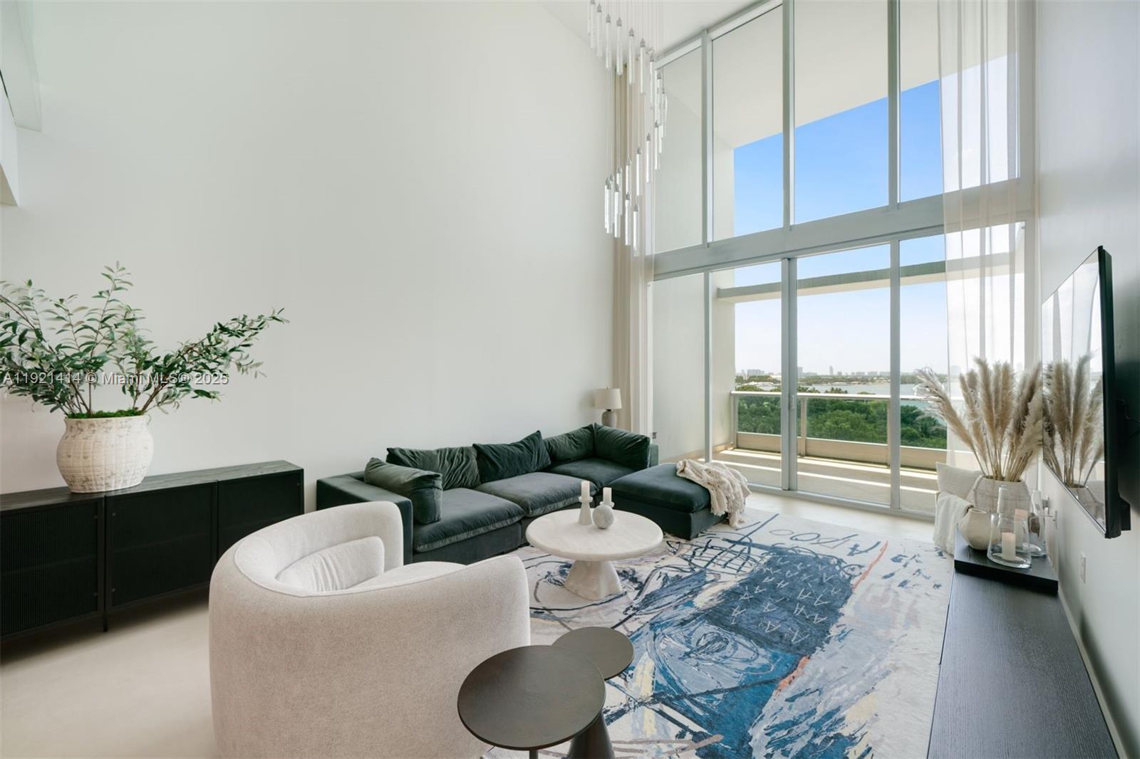 A modern living room features double-height windows, a dark sectional sofa, and a patterned rug — 900 Biscayne Blvd # 905, Miami FL 33132, MIAMI, FL