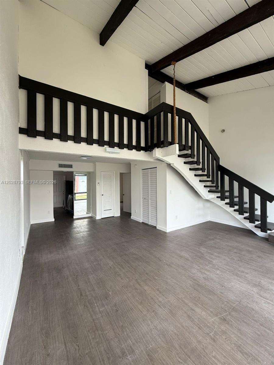 A living room features dark wood-look flooring, a staircase with a black railing, and vaulted ceilings — 14310 NE 5th Pl, Miami FL 33161, MIAMI, FL