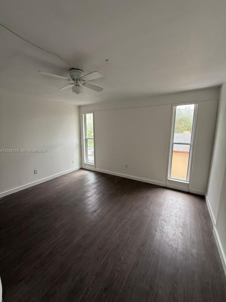 An empty room features white walls, dark wood-look flooring, a ceiling fan, and two windows — 14310 NE 5th Pl, Miami FL 33161, MIAMI, FL