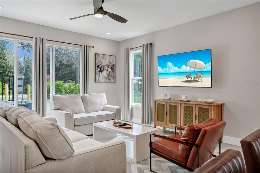 A living room features a light-colored sofa, a brown leather chair, and a wall-mounted television — 7833 SPECTRUM DRIVE, KISSIMMEE, FL