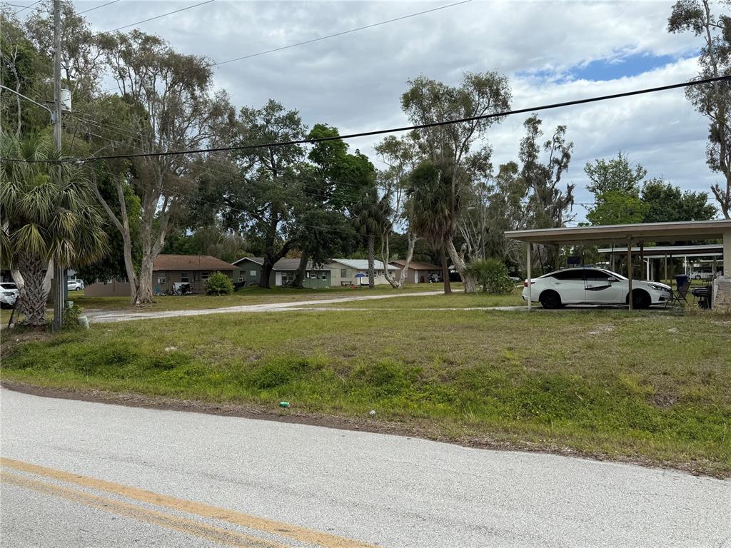A grassy lot features a white sedan parked under a carport near several small houses — 6797 54TH AVENUE N, ST PETERSBURG, FL