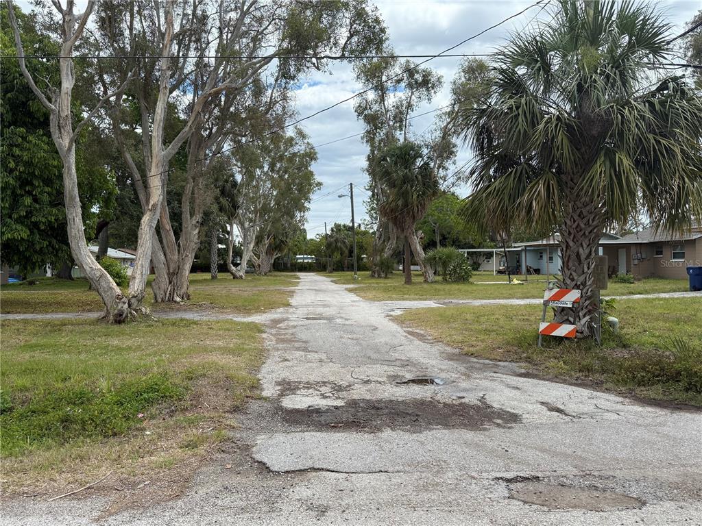 A weathered, unpaved road stretches between grassy lots lined with tall trees and palm trees — 6797 54TH AVENUE N, ST PETERSBURG, FL