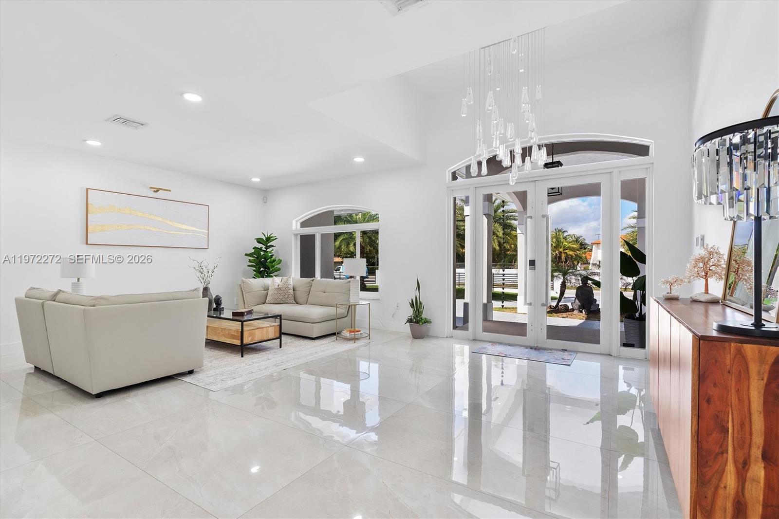 A bright living room features white tile floors, a modern chandelier, and large glass doors — 135 SW 125th Ave, Miami FL 33184, MIAMI, FL