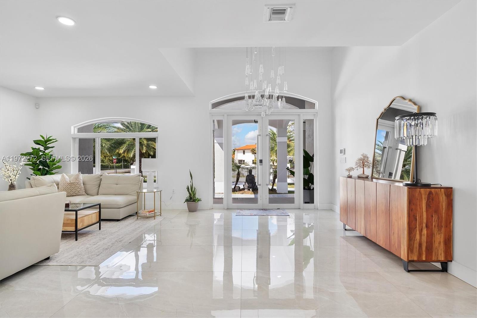 A bright, open-concept living room features white tile floors, a modern chandelier, and glass doors — 135 SW 125th Ave, Miami FL 33184, MIAMI, FL