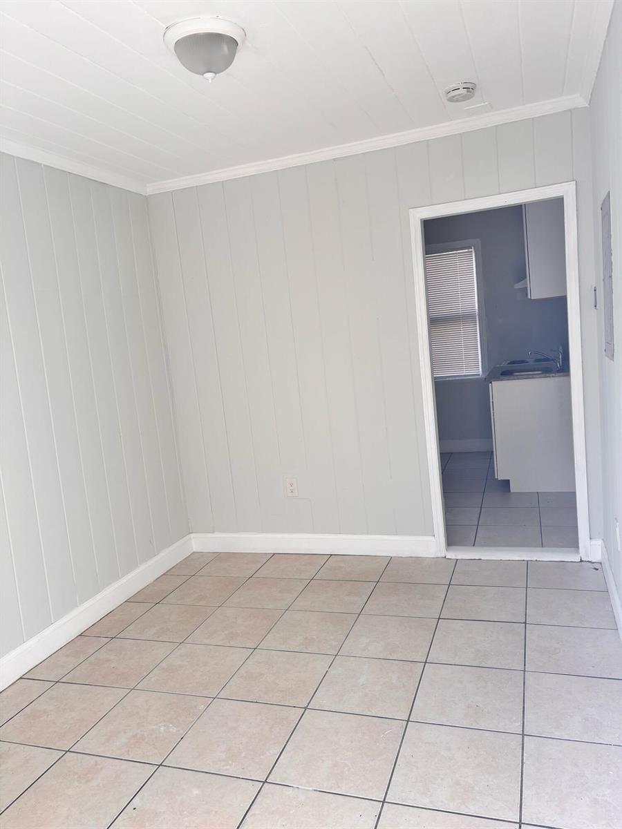 A room with light gray vertical paneling, tile flooring, and a doorway leading to a kitchen — 817 7th Street, West Palm Beach FL 33401, WEST PALM BEACH, FL