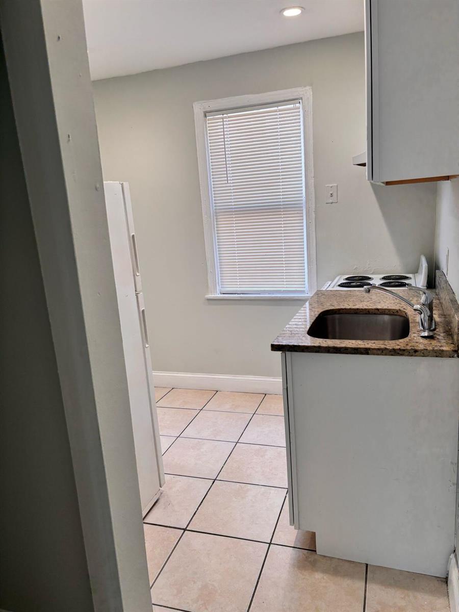A small kitchen features a stainless steel sink, granite countertop, white cabinets, and tile flooring — 817 7th Street, West Palm Beach FL 33401, WEST PALM BEACH, FL