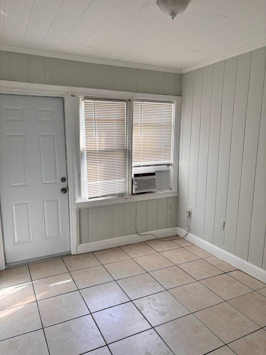 A room with light-colored wood paneling, tiled flooring, a white door, and a window unit — 817 7th Street, West Palm Beach FL 33401, WEST PALM BEACH, FL