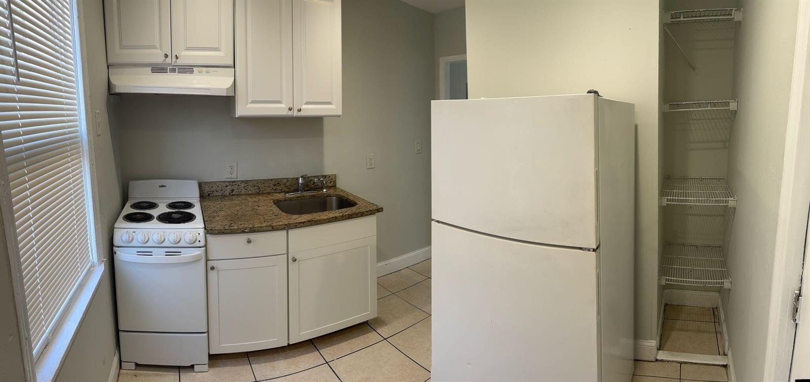 A small kitchen features white cabinets, a white stove, a refrigerator, and open wire shelving — 817 7th Street, West Palm Beach FL 33401, WEST PALM BEACH, FL