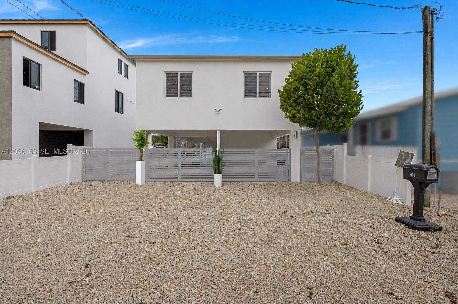 A white two-story house features a gravel driveway, a fenced yard, and a covered carport — 410 Bowie Ln, Key Largo FL 33037, KEY LARGO, FL