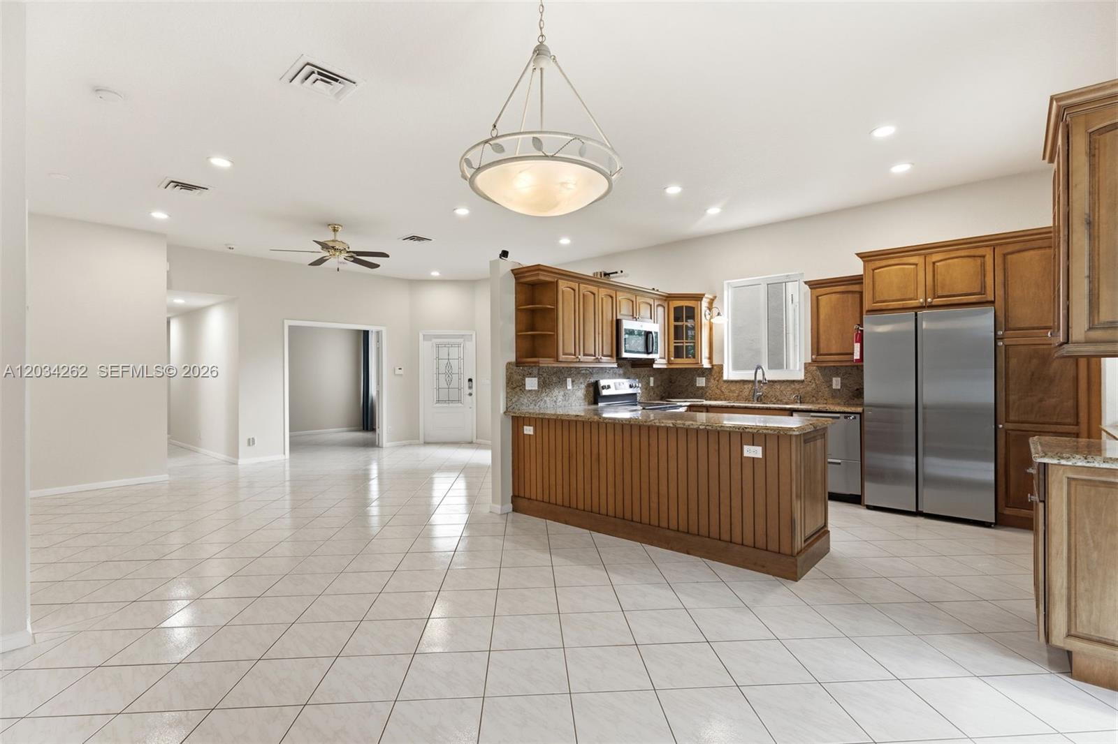 A kitchen with wood cabinets and a granite-topped island opens into a tiled living area — 6530 Sandpiper Dr, Coconut Creek FL 33073, COCONUT CREEK, FL
