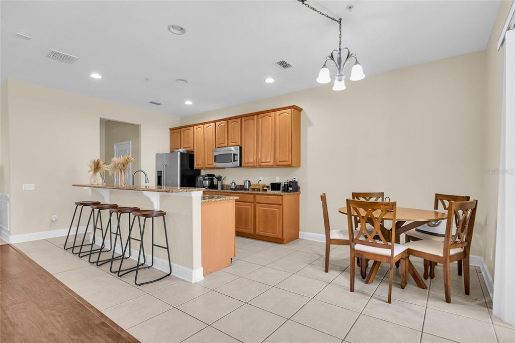 A kitchen with wood cabinets, a breakfast bar with stools, and a dining area — 6380 CONEJO TERRACE UNIT 104, ORLANDO, FL