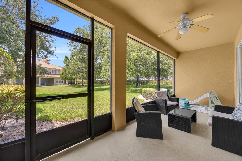 A screened-in patio features wicker furniture, a ceiling fan, and views of a grassy backyard — 6380 CONEJO TERRACE UNIT 104, ORLANDO, FL