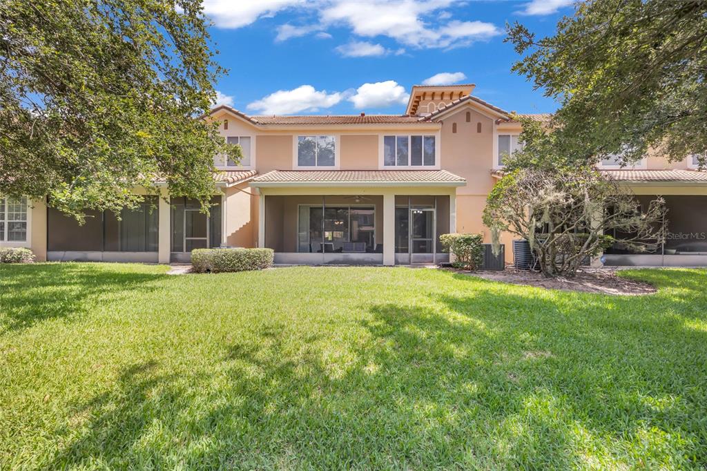 The rear exterior of a two-story house features a screened-in patio and a grassy yard — 6380 CONEJO TERRACE UNIT 104, ORLANDO, FL
