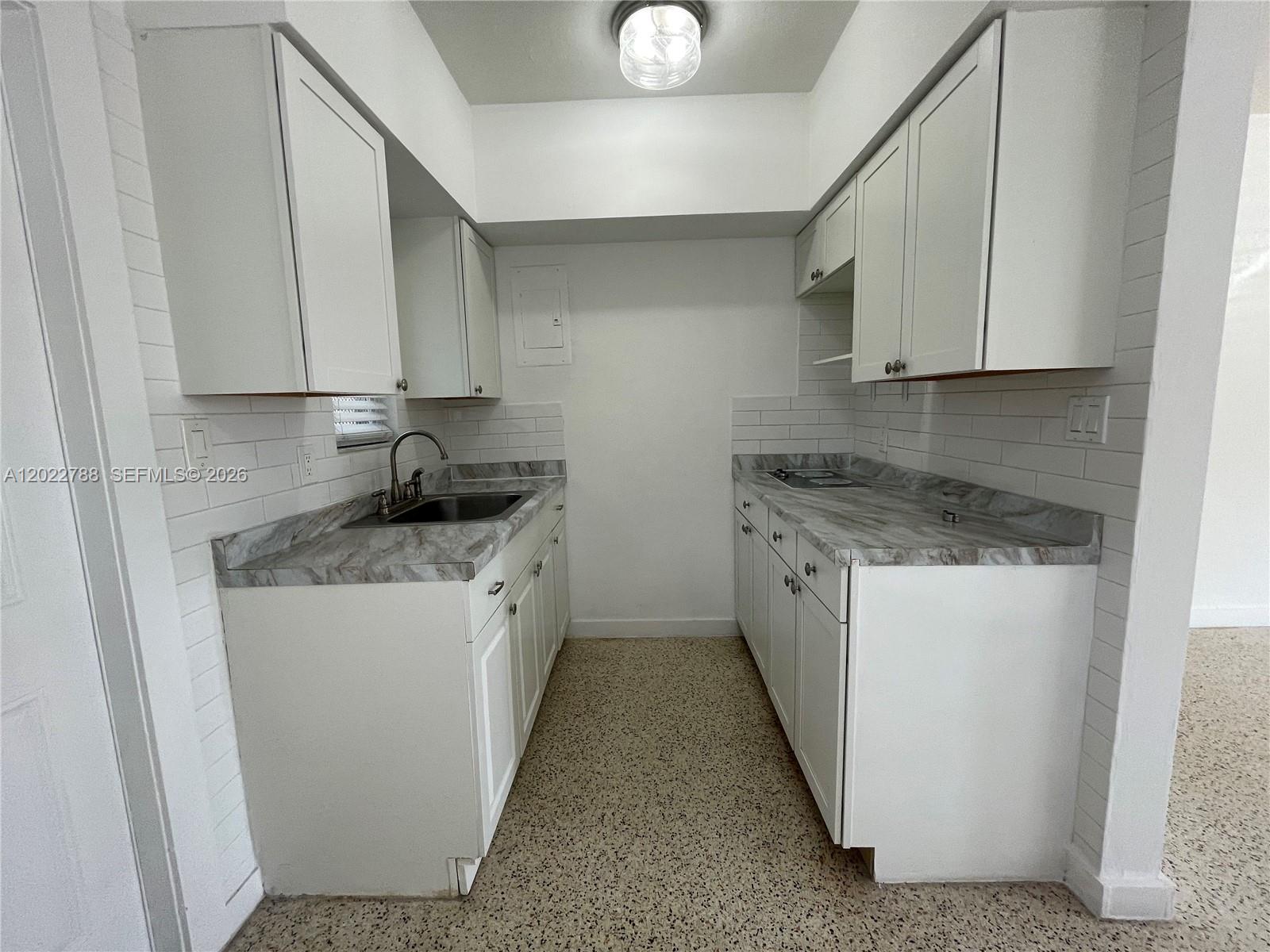 A galley kitchen features white cabinets, marble-patterned countertops, and a white subway tile backsplash — 940 SW 4th ave # 1, Miami FL 33130, MIAMI, FL