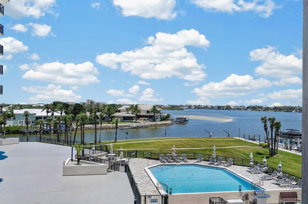 An elevated view of a swimming pool, grassy lawn, and a bay with distant houses — 503 N CAUSEWAY UNIT 2020, NEW SMYRNA BEACH, FL