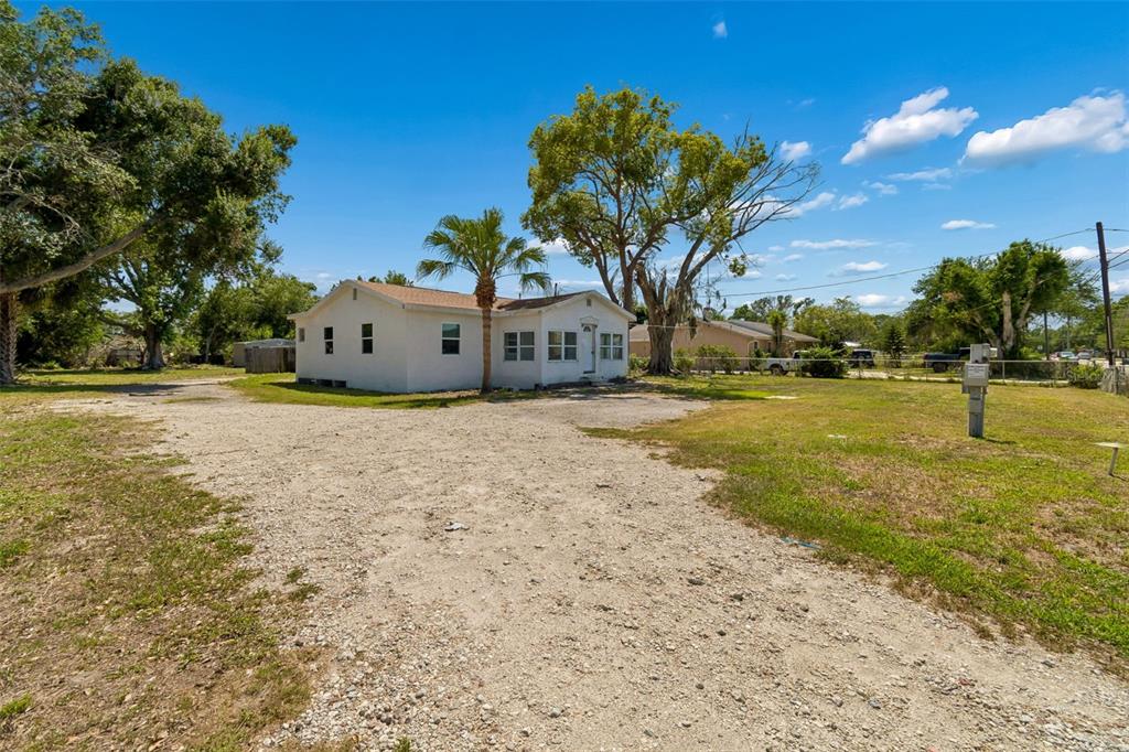 A white, single-story house sits on a large, unpaved gravel lot with several mature trees — 1611 E SHELL POINT ROAD, RUSKIN, FL