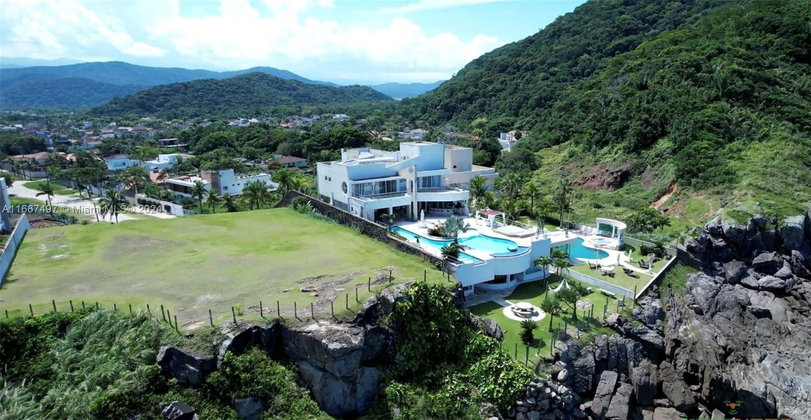 An aerial view shows a modern white house with a pool situated on a rocky cliff — 198 Passeio ave, SP 11444-380, SP