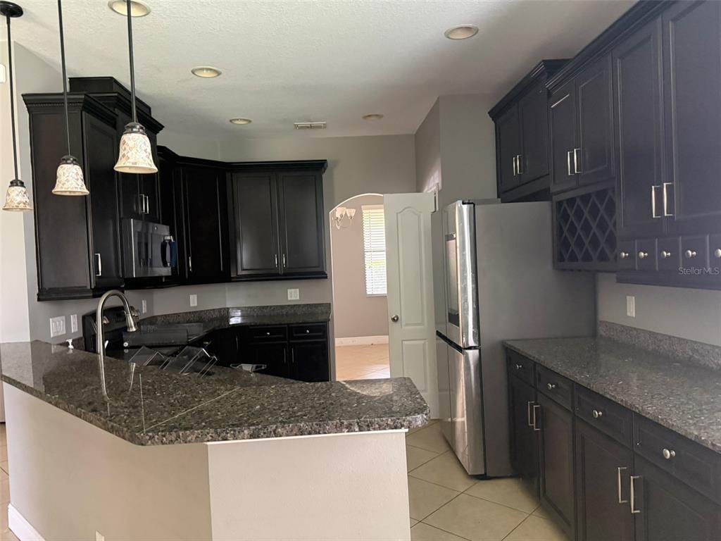 A kitchen features dark wood cabinets, granite countertops, stainless steel appliances, and a breakfast bar — 1863 ALTAVISTA CIRCLE, LAKELAND, FL