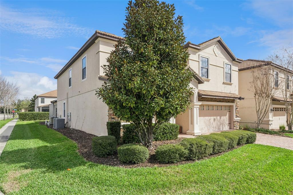 A two-story beige house with a garage and landscaping sits on a grassy lot — 1430 MOON VALLEY DRIVE, DAVENPORT, FL