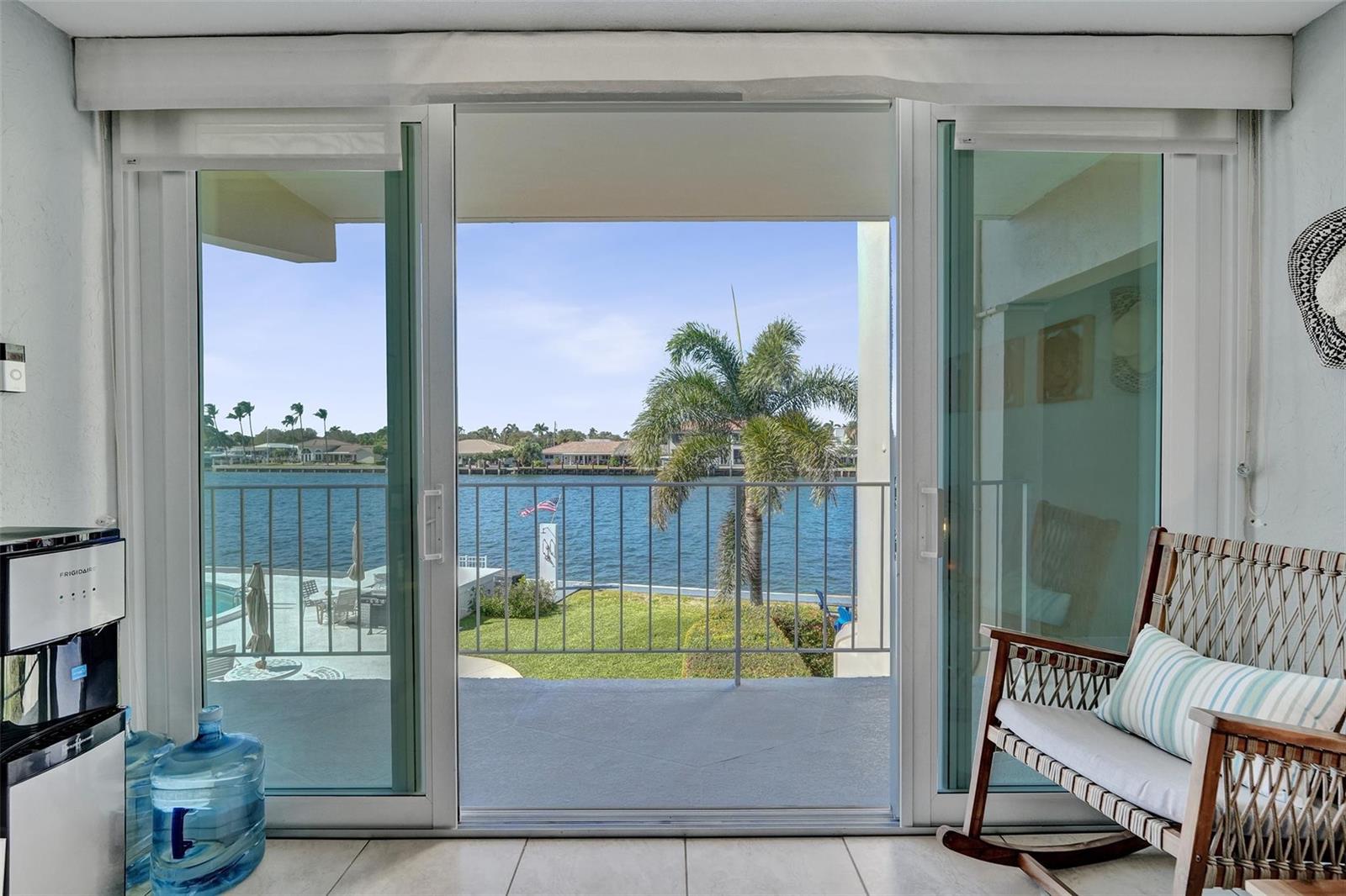 A room with a water cooler and rocking chair looks out through sliding doors to a balcony — 801 N Riverside Drive # 4b, Pompano Beach FL 33062, POMPANO BEACH, FL