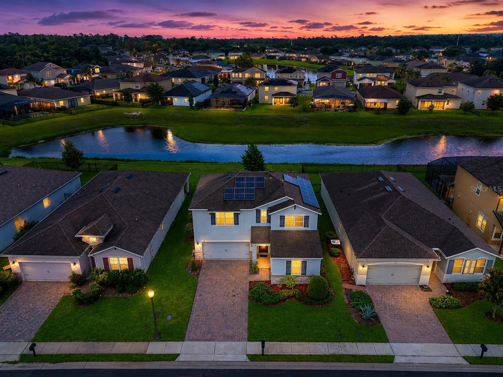 An aerial view shows a suburban neighborhood with houses, a pond, and a sunset sky — 276 DRAYTON AVENUE, DAVENPORT, FL