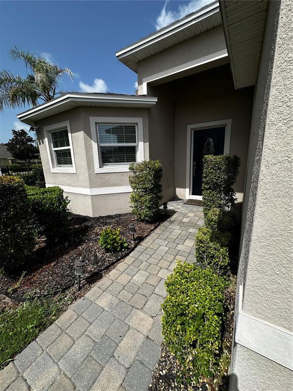 A paved walkway leads to the front entrance of a beige house with trimmed hedges — 262 LAKE MARIANA PLACE, AUBURNDALE, FL