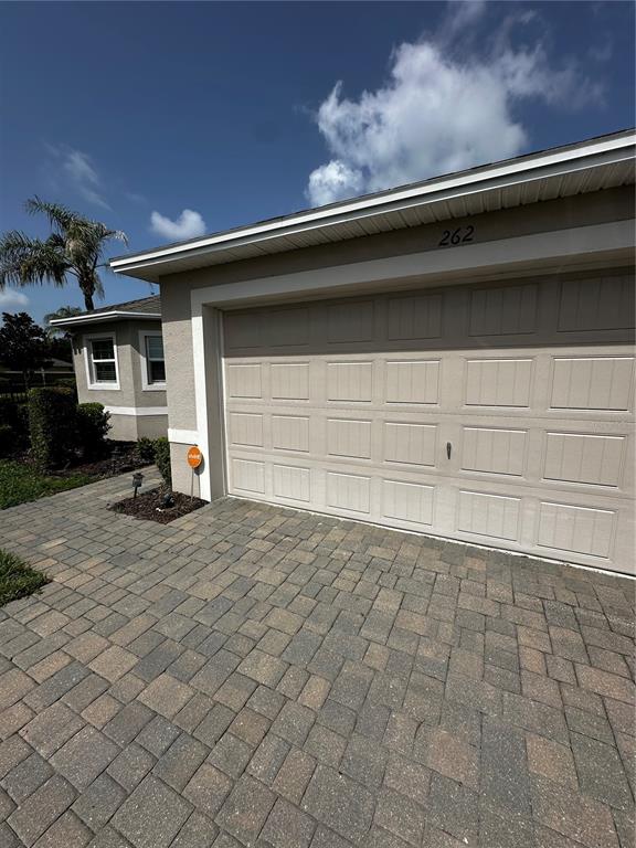 A beige garage with a paved driveway and a palm tree in the background — 262 LAKE MARIANA PLACE, AUBURNDALE, FL