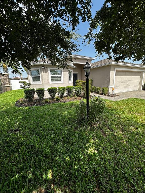 A single-story house with a tan exterior, a two-car garage, and a front yard lamp — 262 LAKE MARIANA PLACE, AUBURNDALE, FL