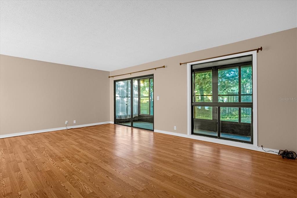 An empty living room features light brown walls, wood-look flooring, and large sliding glass doors — 411 SHEOAH BOULEVARD UNIT 43, WINTER SPRINGS, FL