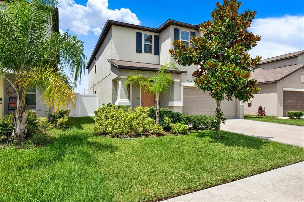 A two-story suburban house with a tan stucco exterior, a garage, and front yard landscaping — 7505 SAMUEL IVY DRIVE, TAMPA, FL