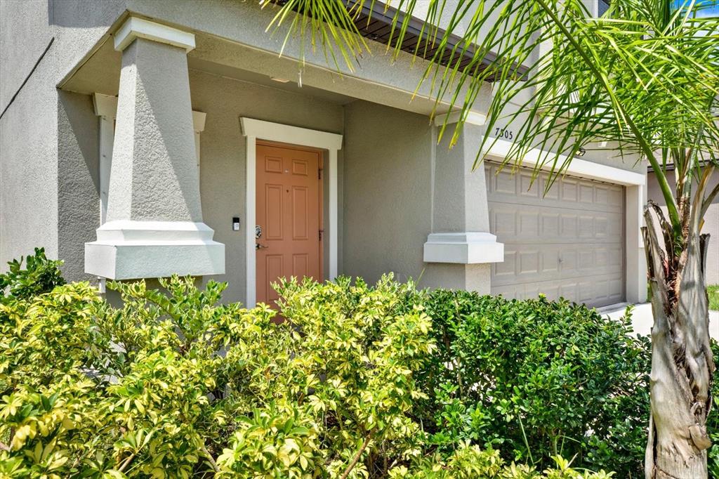 A tan front door is framed by two white pillars and a garage entrance — 7505 SAMUEL IVY DRIVE, TAMPA, FL