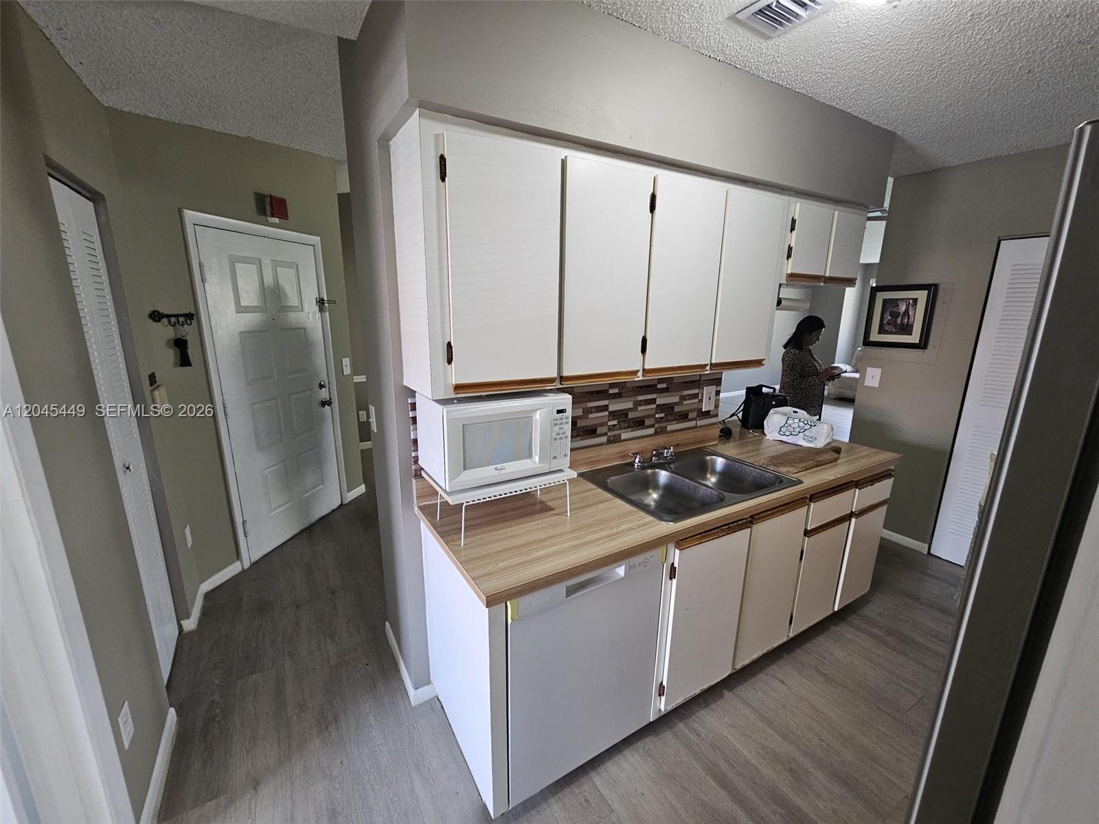 A kitchen features white cabinets, wood-look laminate countertops, a double sink, and a microwave — 18306 NW 68th Ave # H, Hialeah FL 33015, HIALEAH, FL