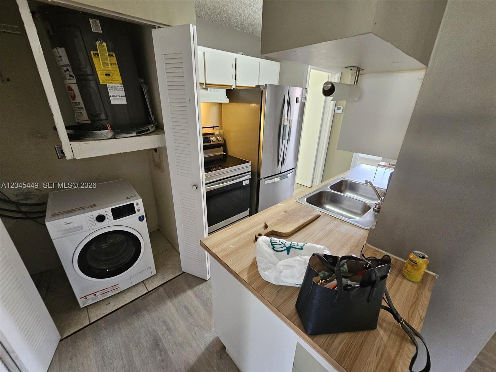 A kitchen features a laundry closet with a water heater, stainless appliances, and wood-look countertops — 18306 NW 68th Ave # H, Hialeah FL 33015, HIALEAH, FL