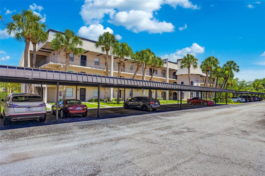 A multi-story apartment building features covered parking spaces and palm trees in front — 8693 BARDMOOR BOULEVARD UNIT 301B, LARGO, FL