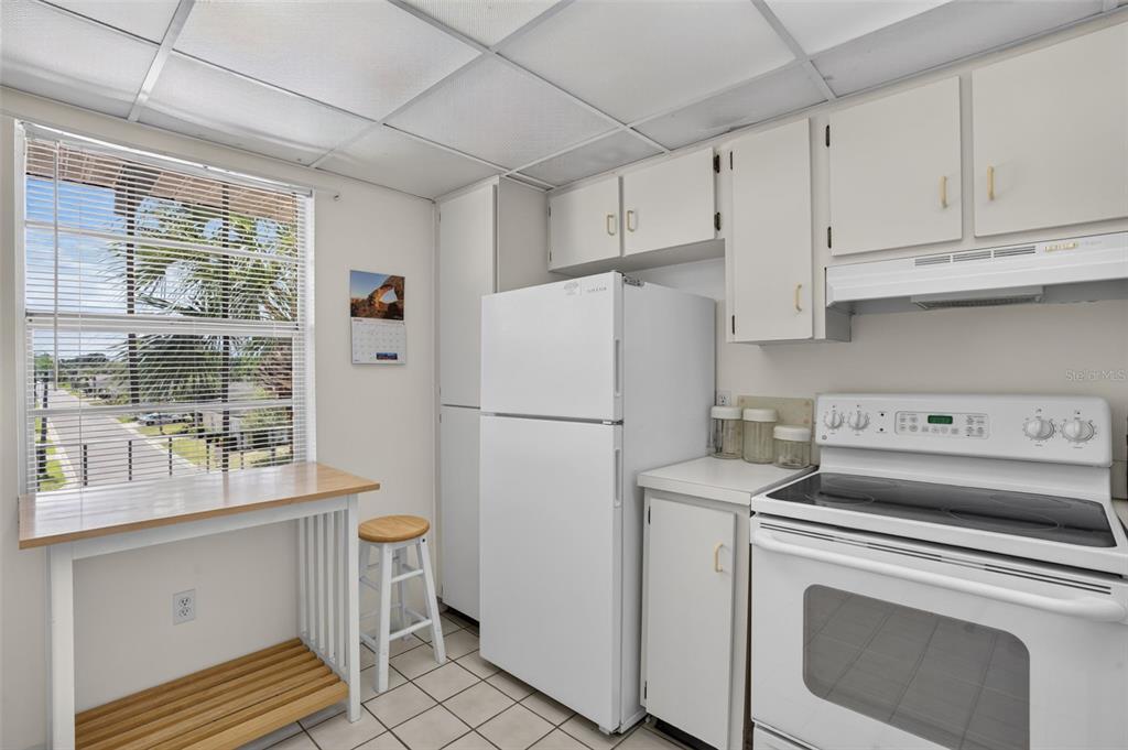 A kitchen features white appliances, white cabinets, tiled floors, and a small wooden breakfast table — 8693 BARDMOOR BOULEVARD UNIT 301B, LARGO, FL