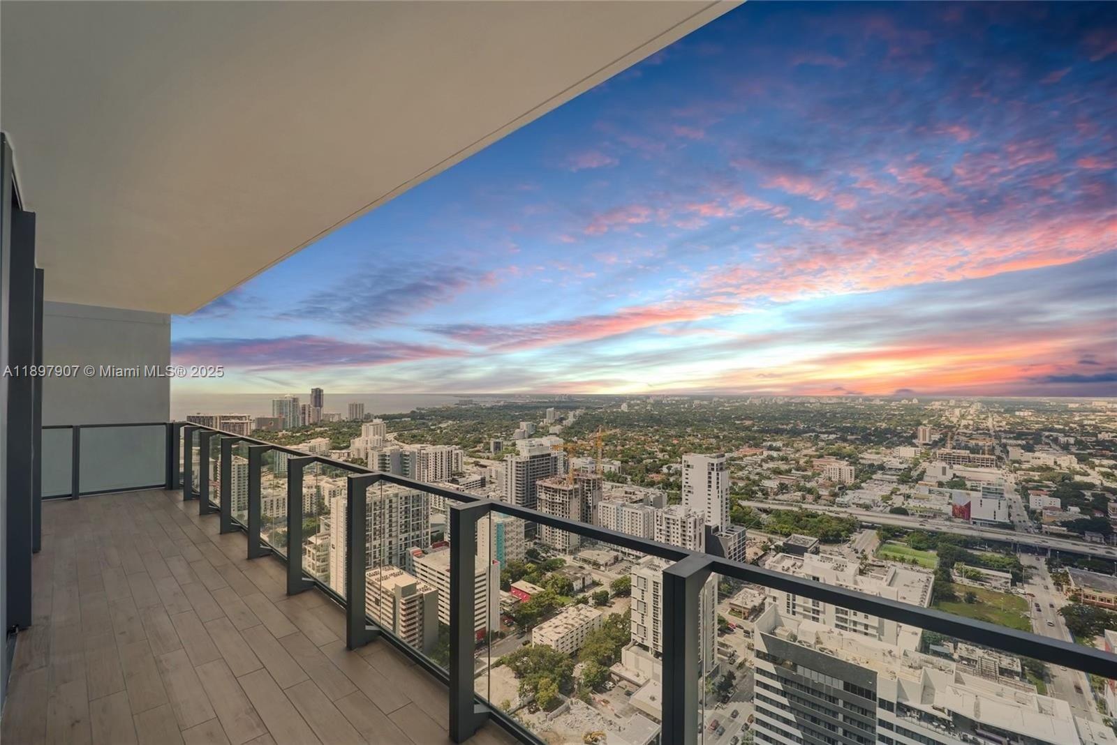 A high-rise balcony with glass railings overlooks a city skyline at sunset — 88 SW 7th St # 3910, Miami FL 33130, MIAMI, FL