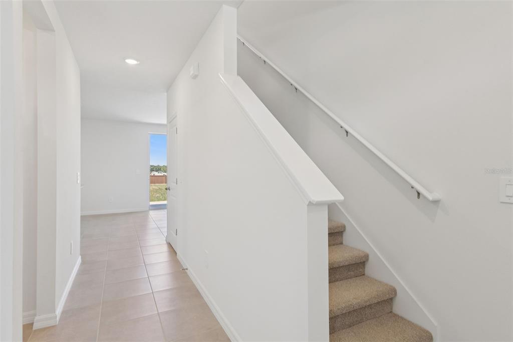 A hallway with tile flooring leads to an exterior door next to carpeted stairs — 12589 HOMELAND DRIVE, DADE CITY, FL